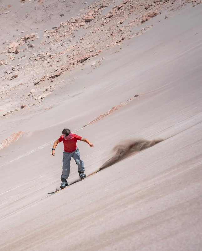 Persona bajando una duna en sandboard, levantando arena a su paso